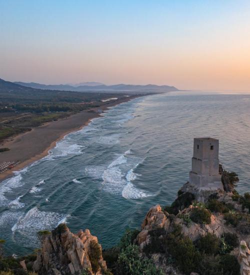 Vue côtière au coucher du soleil avec tour sur falaise.