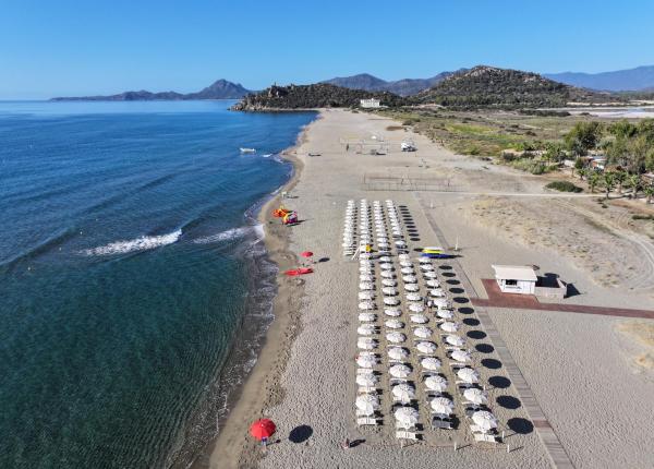 Plage de sable avec parasols et mer calme, paysage montagneux en arrière-plan.