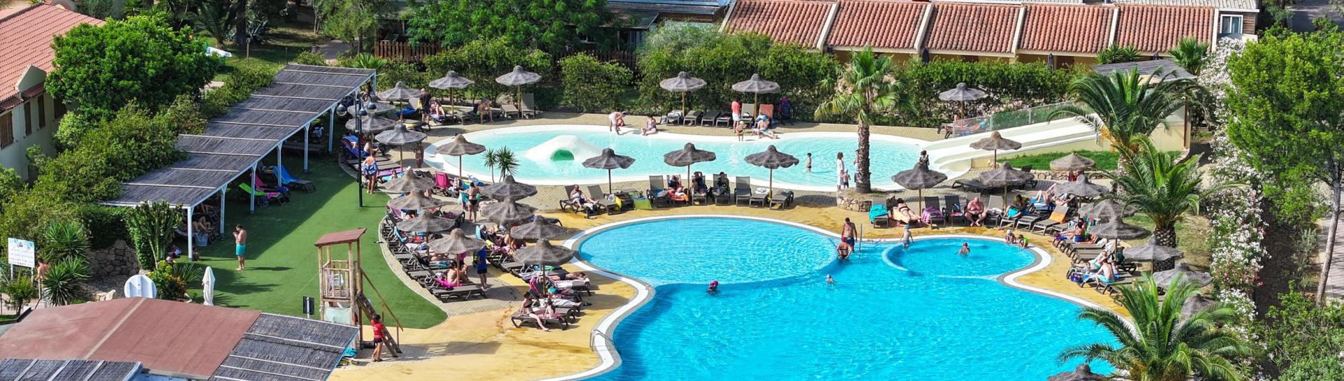 Piscina all'aperto con sdraio e ombrelloni, circondata da alberi e fiori.