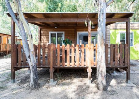 Cabane en bois avec véranda et clôture, entourée de nature.