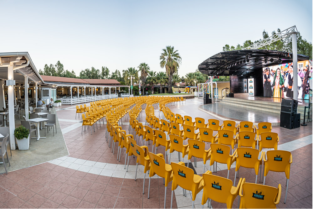 Scène extérieure avec des chaises jaunes disposées pour un événement en soirée.